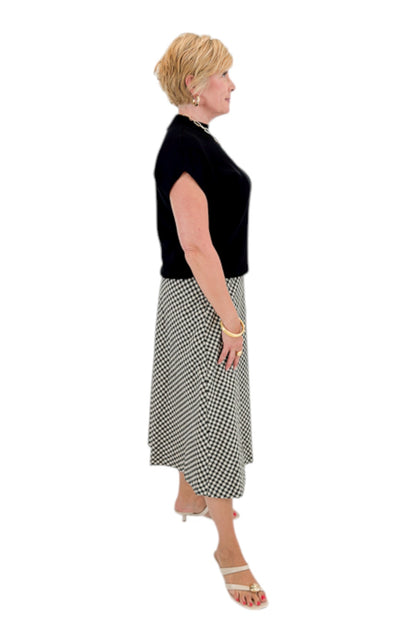 Side view of woman wearing Swagger Boutique’s Black Shirred Cap Sleeve Sweater with Black &amp; White Plaid Midi Skirt against white studio background.