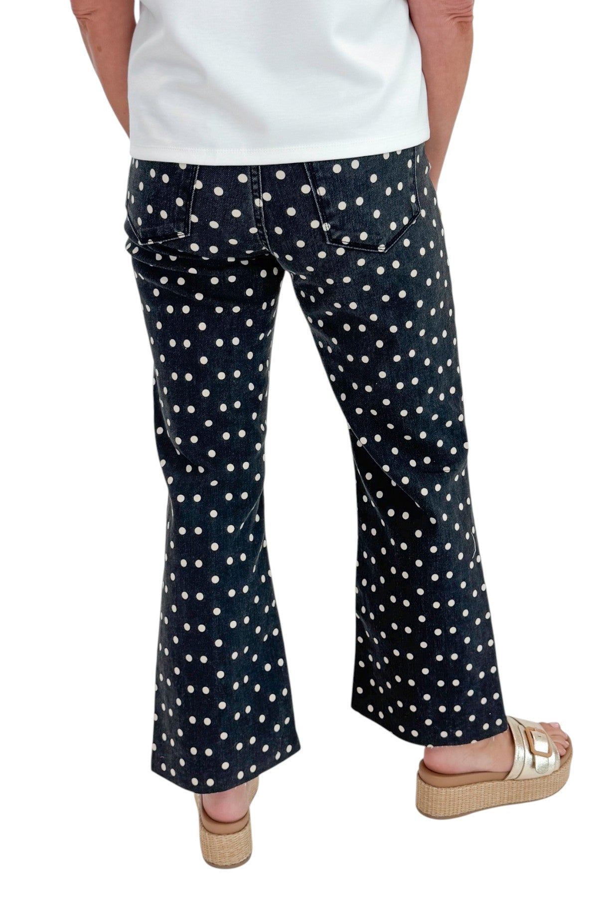 Back view of woman wearing Swagger Boutique’s Black &amp; White Polka Dot Crop Flare Jeans by Just Black Denim with top against white studio background.