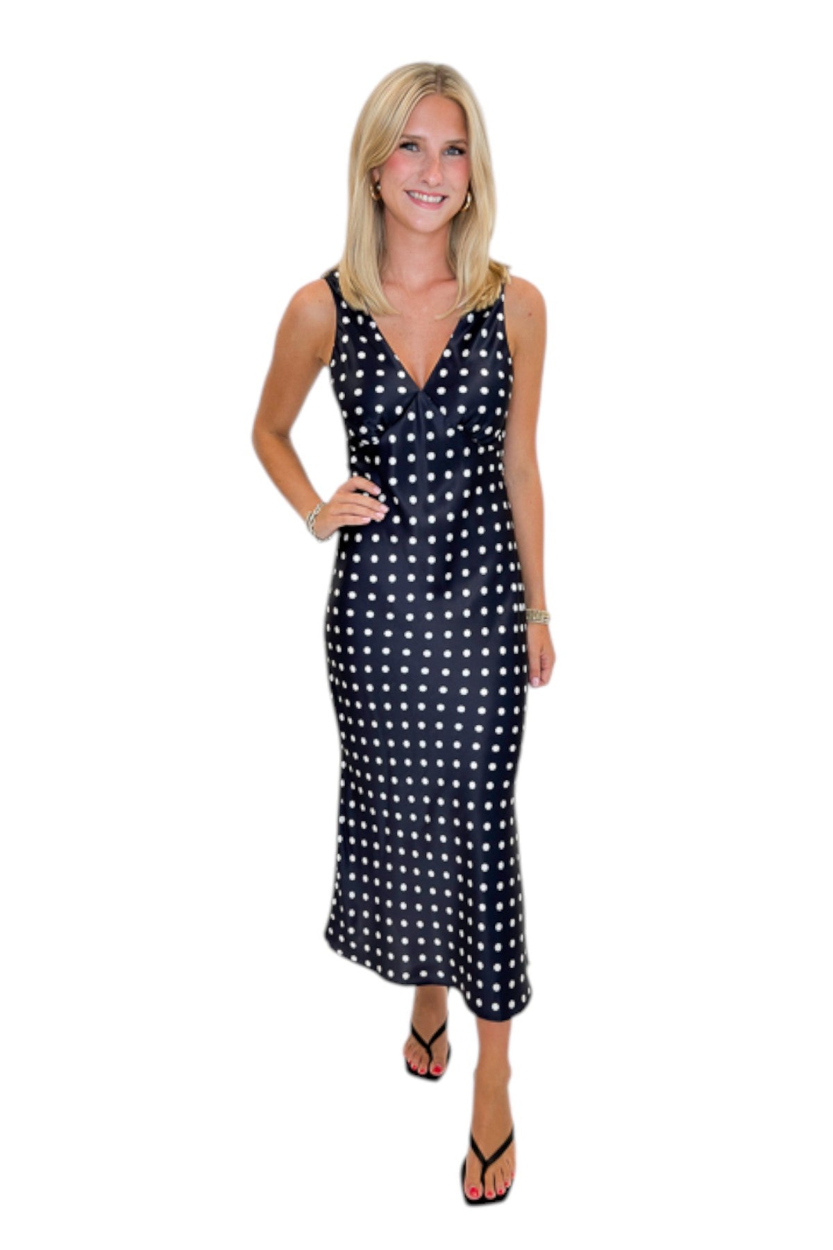 Front view of woman wearing Swagger Boutique’s Black &amp; White Polka Dot Satin Midi Dress with heels against white studio background.