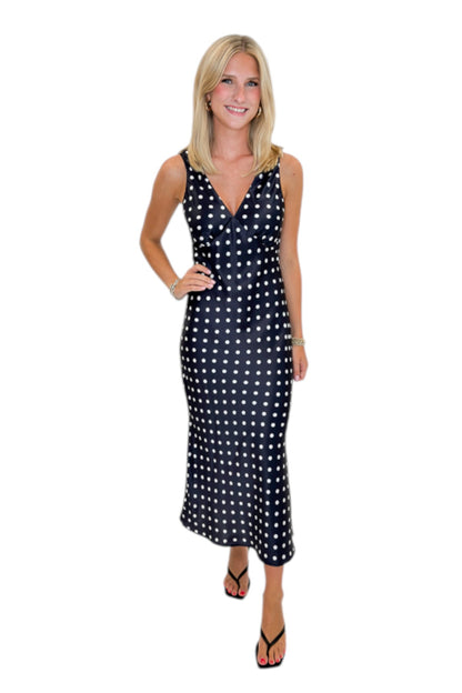 Front view of woman wearing Swagger Boutique’s Black &amp; White Polka Dot Satin Midi Dress with heels against white studio background.