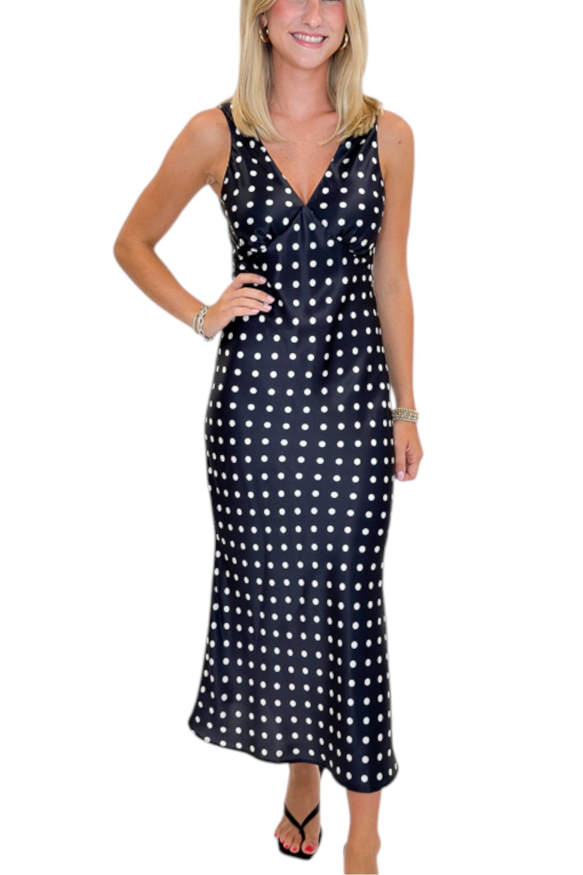 Front detail view of woman wearing Swagger Boutique’s Black &amp; White Polka Dot Satin Midi Dress with heels against white studio background.