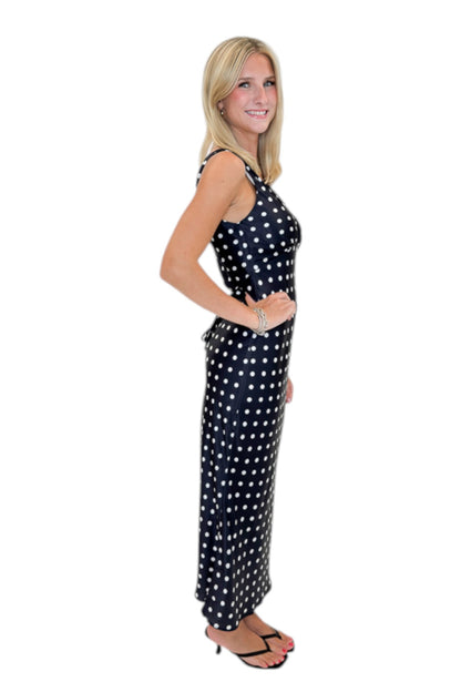 Side view of woman wearing Swagger Boutique’s Black &amp; White Polka Dot Satin Midi Dress with heels against white studio background.