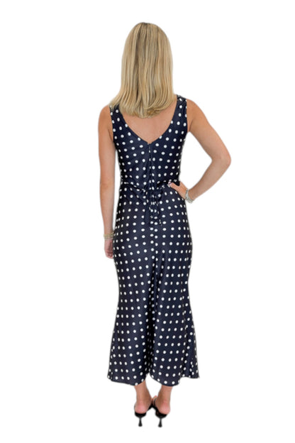 Back view of woman wearing Swagger Boutique’s Black &amp; White Polka Dot Satin Midi Dress with heels against white studio background.