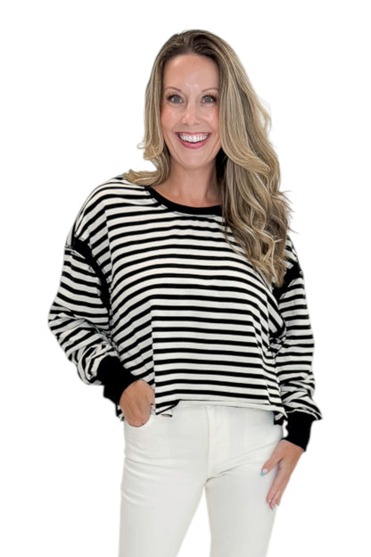 Front view of woman wearing Swagger Boutique’s Black &amp; White Striped Cut Out Back Sweatshirt with jeans against white studio background.