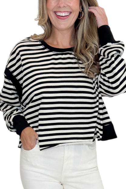 Front detail view of woman wearing Swagger Boutique’s Black &amp; White Striped Cut Out Back Sweatshirt with jeans against white studio background.