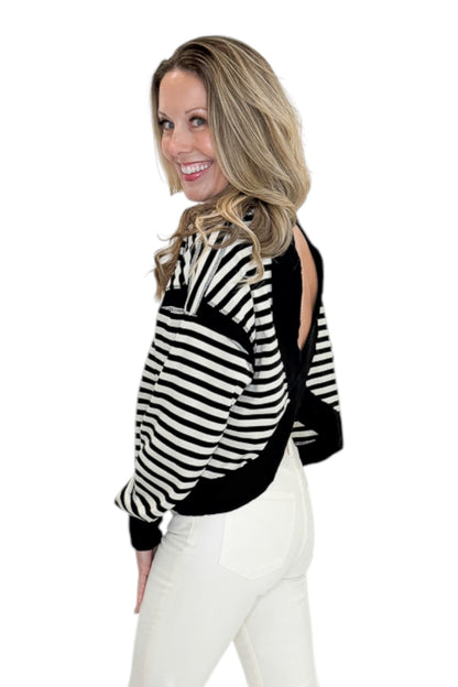 Side view of woman wearing Swagger Boutique’s Black &amp; White Striped Cut Out Back Sweatshirt with jeans against white studio background.