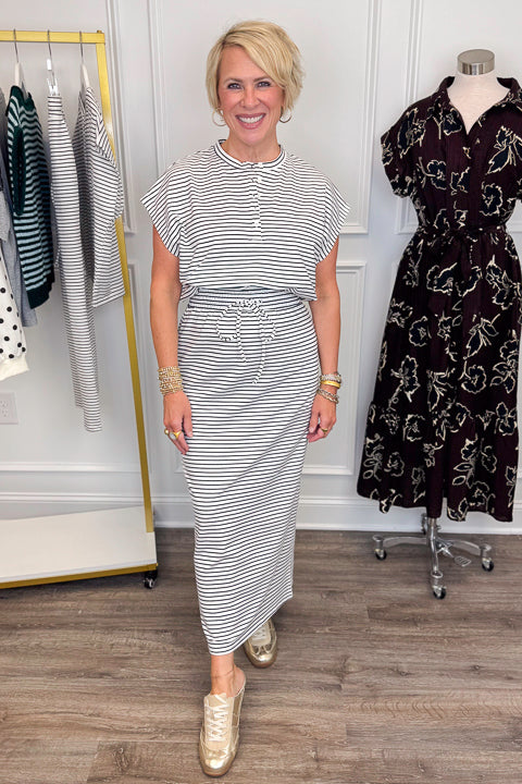 Front view of woman wearing Swagger Boutique’s Black &amp; White Striped Knit Skirt Top with clothing hanging in the background.
