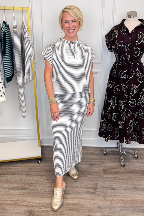 Front view of woman wearing Swagger Boutique’s Black &amp; White Striped Knit Skirt Top with clothing hanging in the background.