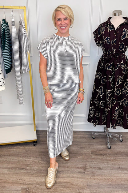 Front view of woman wearing Swagger Boutique’s Black &amp; White Striped Knit Skirt Top with clothing hanging in the background.