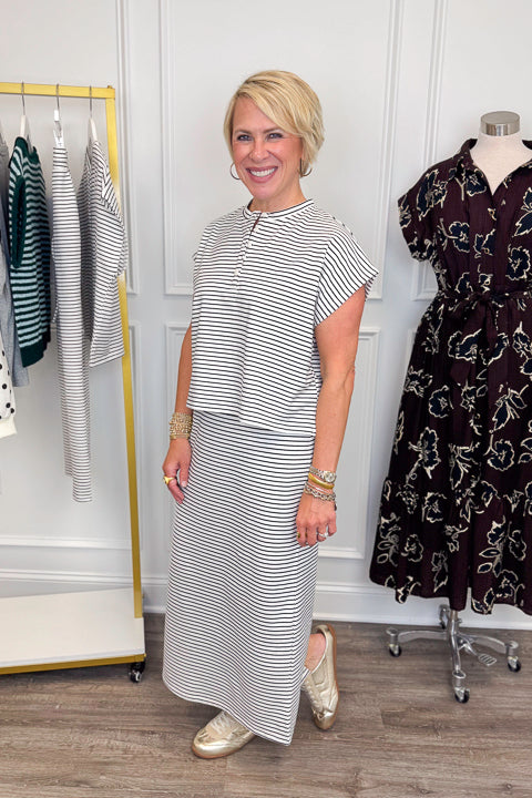 Side view of woman wearing Swagger Boutique’s Black &amp; White Striped Knit Skirt Top with clothing hanging in the background.