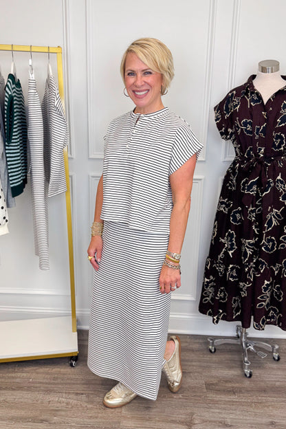 Side view of woman wearing Swagger Boutique’s Black &amp; White Striped Knit Skirt Top with clothing hanging in the background.