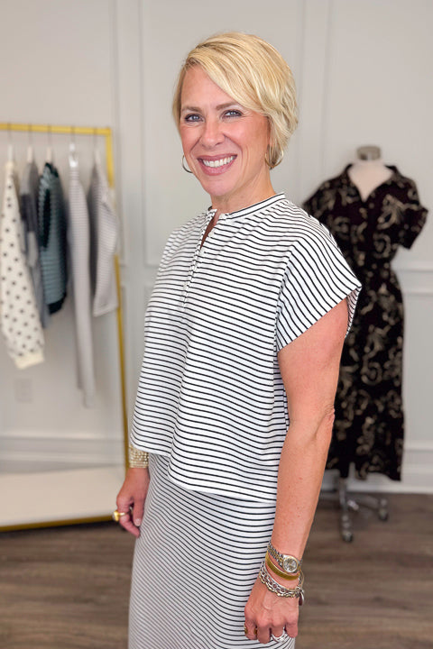 Side view of woman wearing Swagger Boutique’s Black &amp; White Striped Knit Skirt Top with clothing hanging in the background.