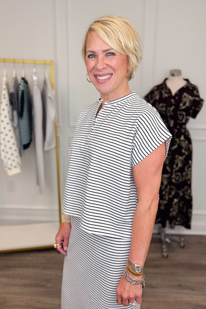 Side view of woman wearing Swagger Boutique’s Black &amp; White Striped Knit Skirt Top with clothing hanging in the background.