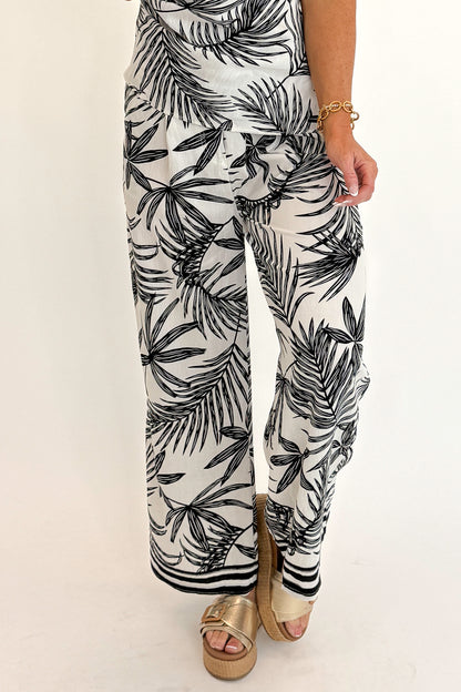 Front detail view of woman wearing Swagger Boutique’s Black &amp; White Tropical Print Strapless Top with matching Black &amp; White Tropical Print Pants against white studio background.