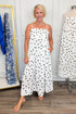 Front view of woman wearing Swagger Boutique’s Black & White Polka Dot Midi Dress with sandals with clothes hanging in the background.