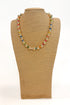 a gold and colorful beaded necklace on a burlap necklace stand with a white background