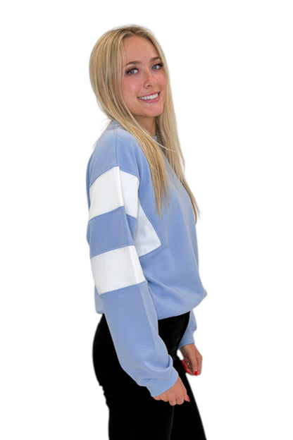 Side view of woman wearing Swagger Boutique’s Blue Color Blocked Long Sleeve Top with jeans against white studio background.