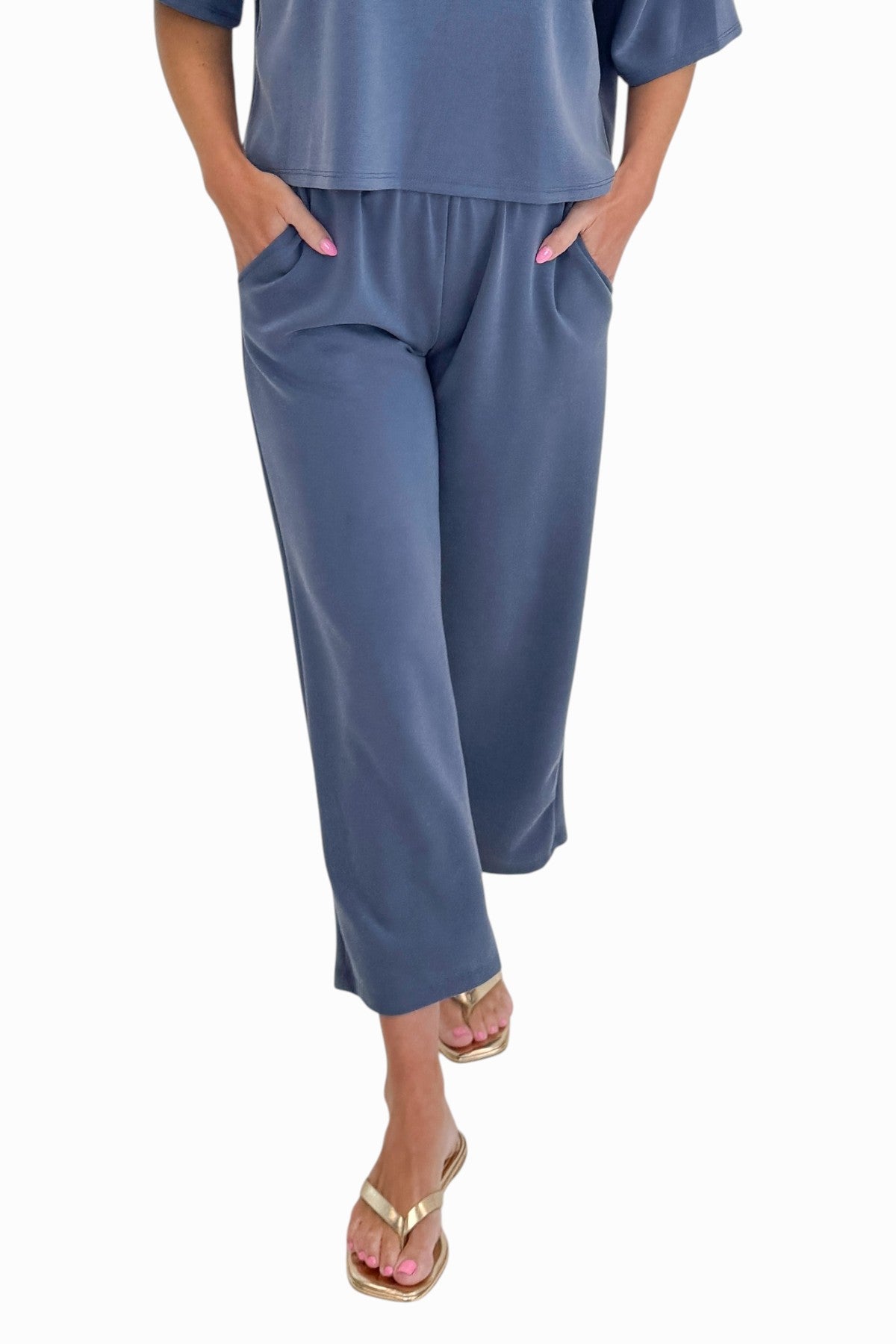 Front view of woman wearing Swagger Boutique’s Blue Cropped Lounge Pants and matching Blue Round Neck Short Sleeve Top against white studio background.