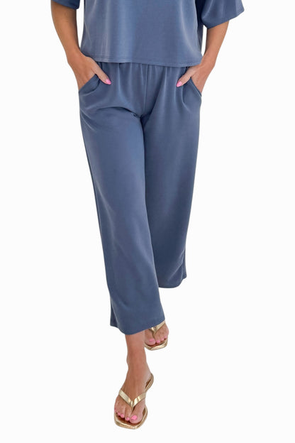 Front view of woman wearing Swagger Boutique’s Blue Cropped Lounge Pants and matching Blue Round Neck Short Sleeve Top against white studio background.