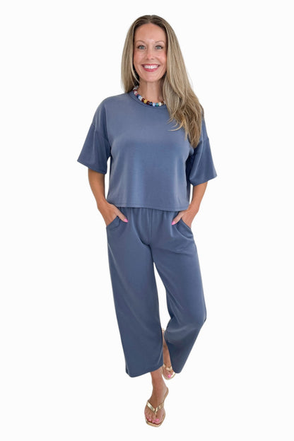 Front view of woman wearing Swagger Boutique’s Blue Cropped Lounge Pants and matching Blue Round Neck Short Sleeve Top against white studio background.