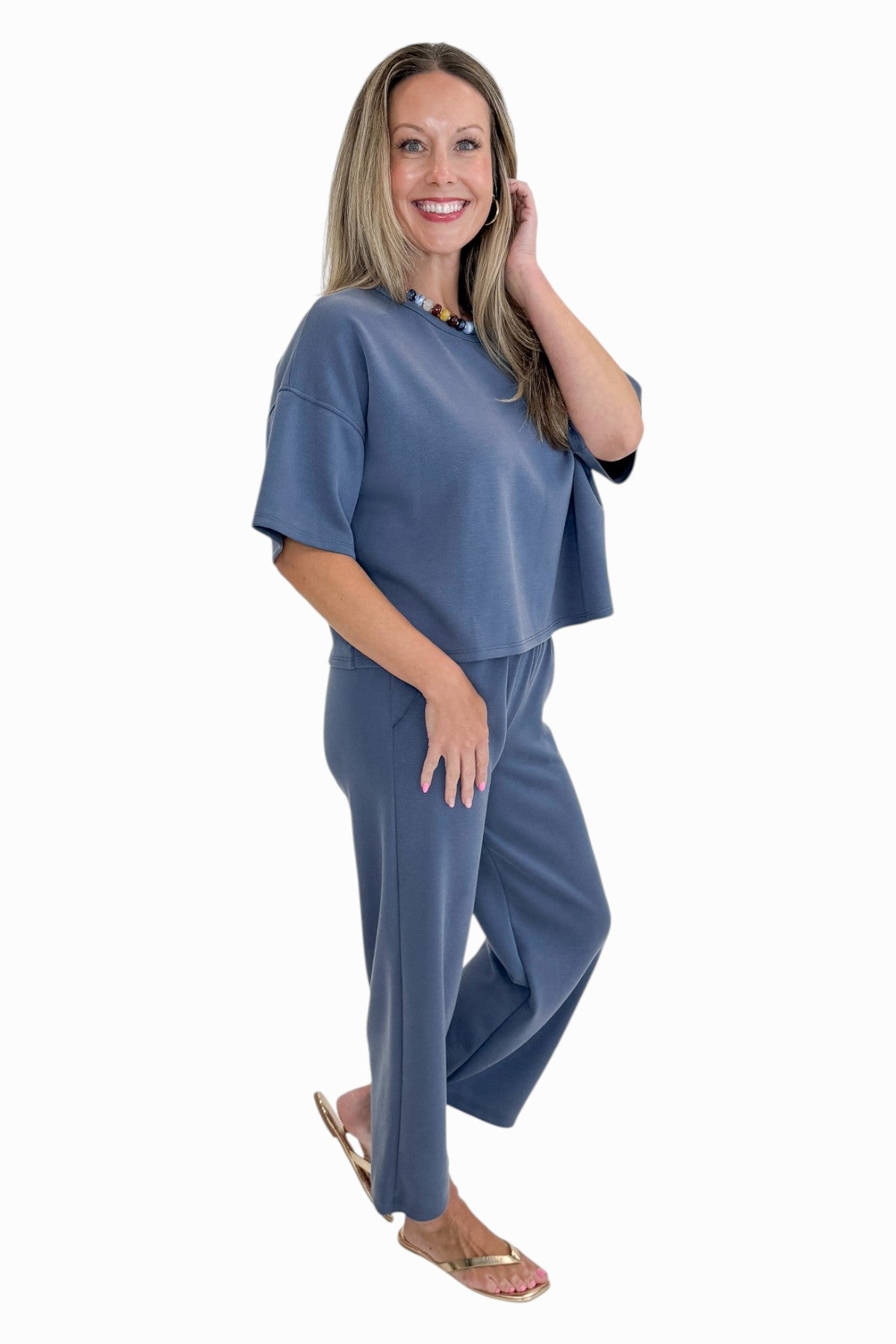 Side view of woman wearing Swagger Boutique’s Blue Cropped Lounge Pants and matching Blue Round Neck Short Sleeve Top against white studio background.