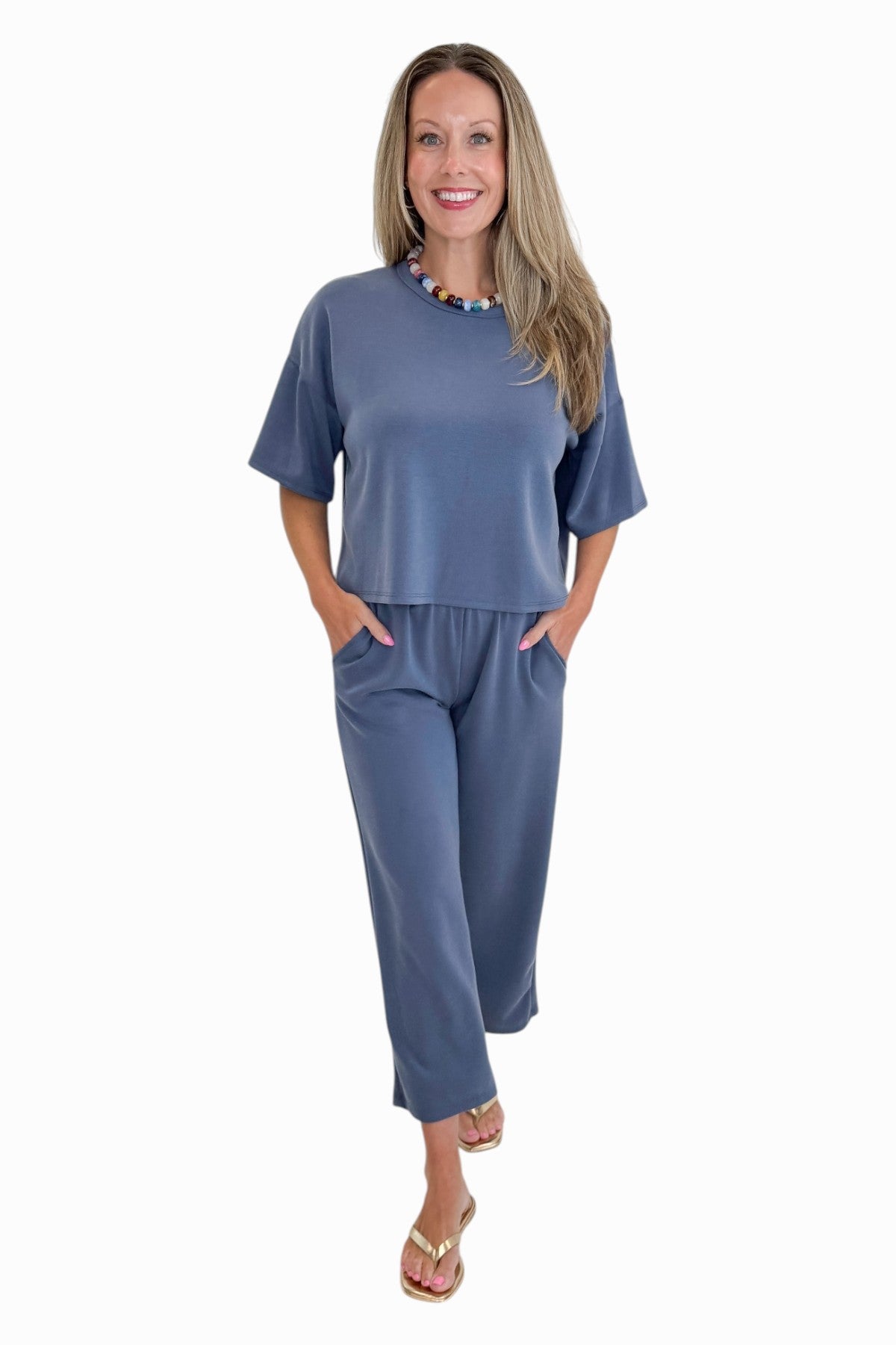 Front view of woman wearing Swagger Boutique’s Blue Cropped Lounge Pants and matching Blue Round Neck Short Sleeve Top against white studio background.
