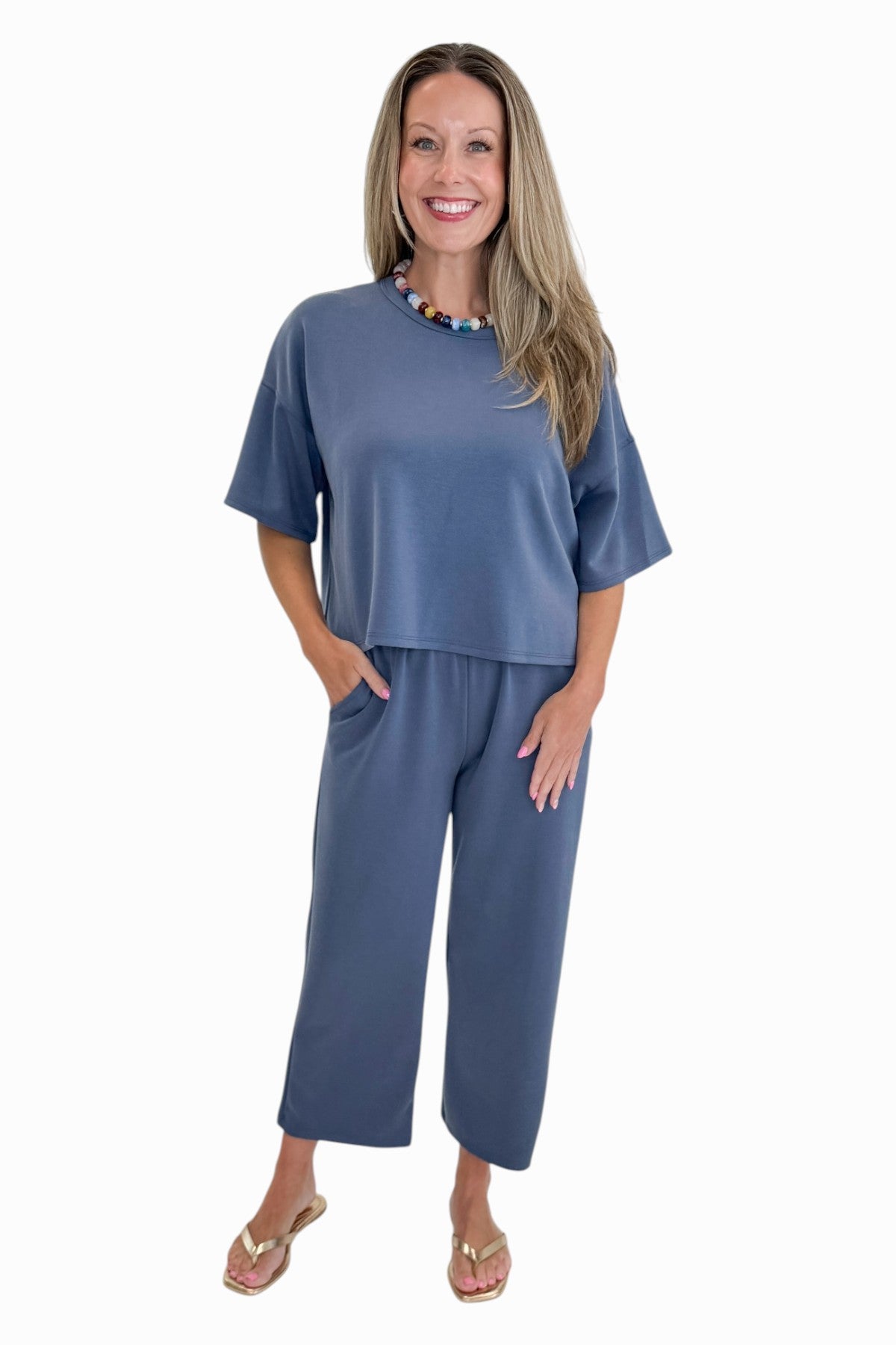 Front view of woman wearing Swagger Boutique’s Blue Cropped Lounge Pants and matching Blue Round Neck Short Sleeve Top against white studio background.