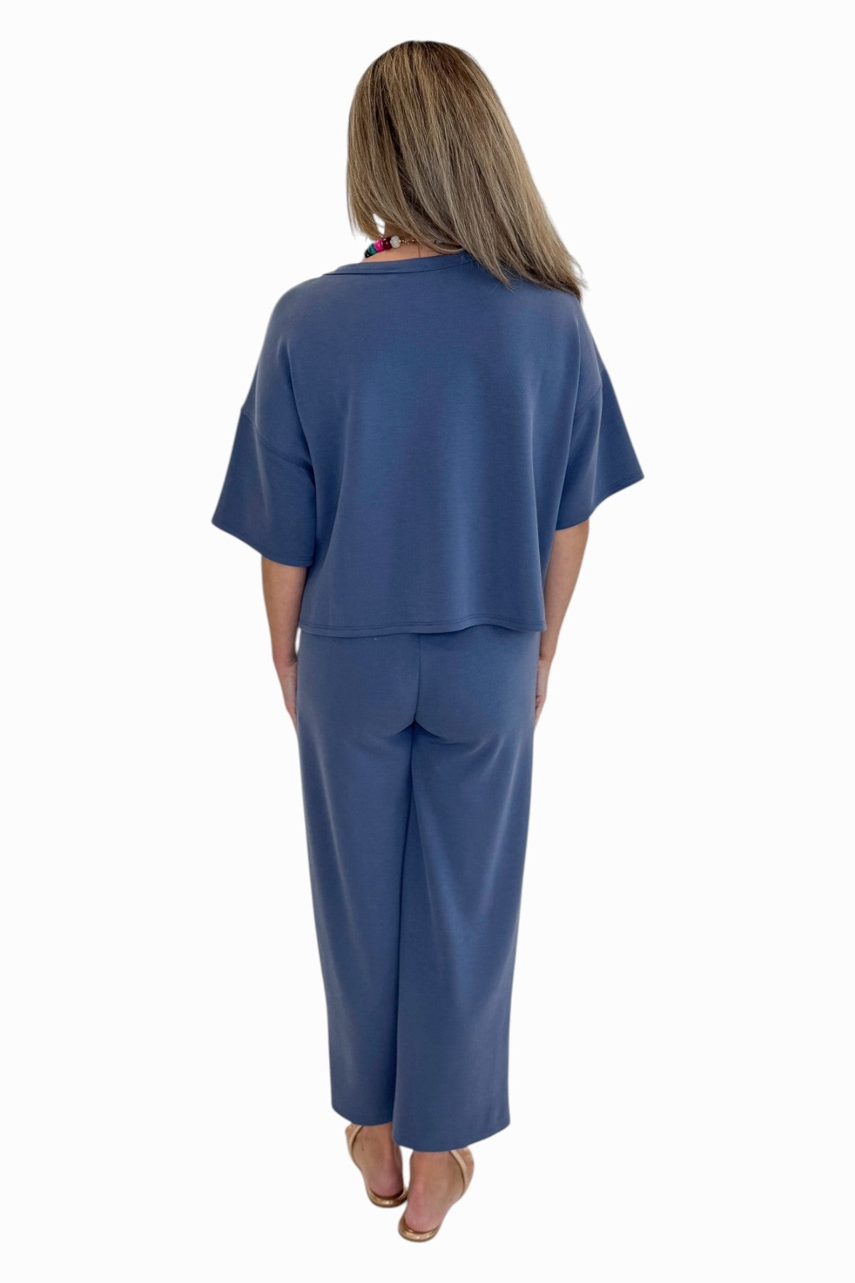 Back view of woman wearing Swagger Boutique’s Blue Cropped Lounge Pants and matching Blue Round Neck Short Sleeve Top against white studio background.
