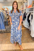 Front view of woman wearing Swagger Boutique’s Blue Floral Puff Sleeve Maxi Dress with sandals at the store.