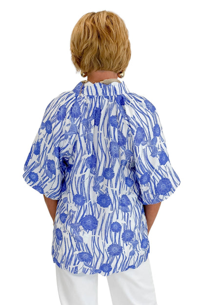 Back view of woman wearing Swagger Boutique’s Blue Floral Puff Sleeve Top with jeans against white studio background.