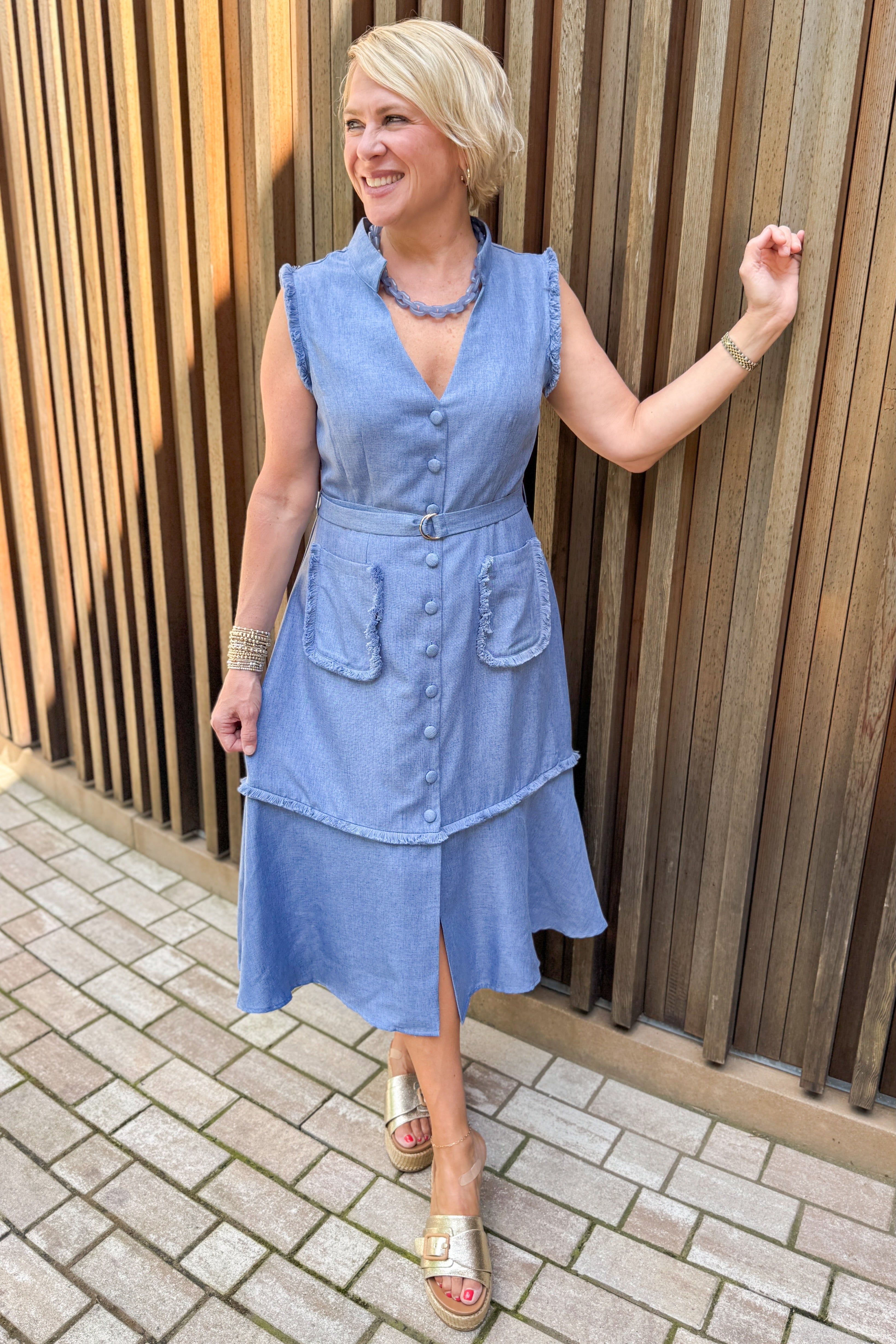 Front view of woman wearing Swagger Boutique’s Blue Fringe Sleeveless Midi Dress with sandals against a wooden background.