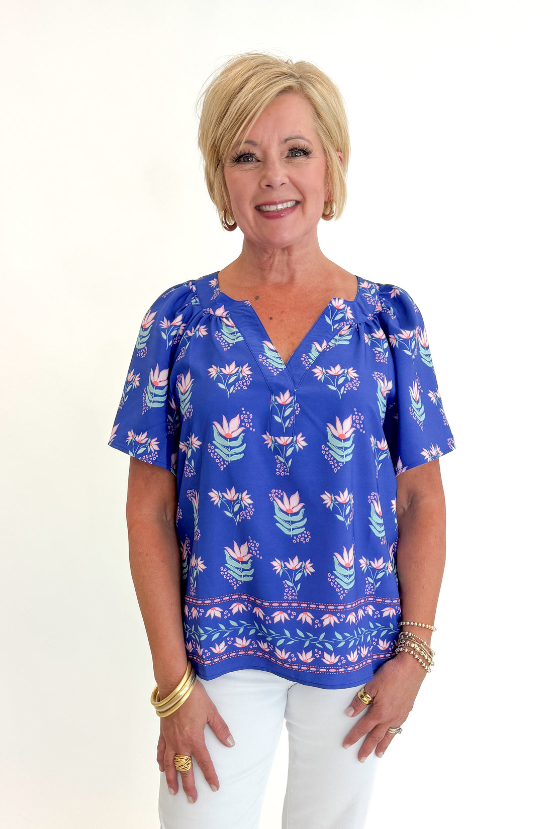 Front view of woman wearing Swagger Boutique’s Blue Petal Print Lori Top by Mary Square with white jeans against white studio background.