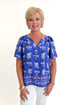Front view of woman wearing Swagger Boutique’s Blue Petal Print Lori Top by Mary Square with white jeans against white studio background.