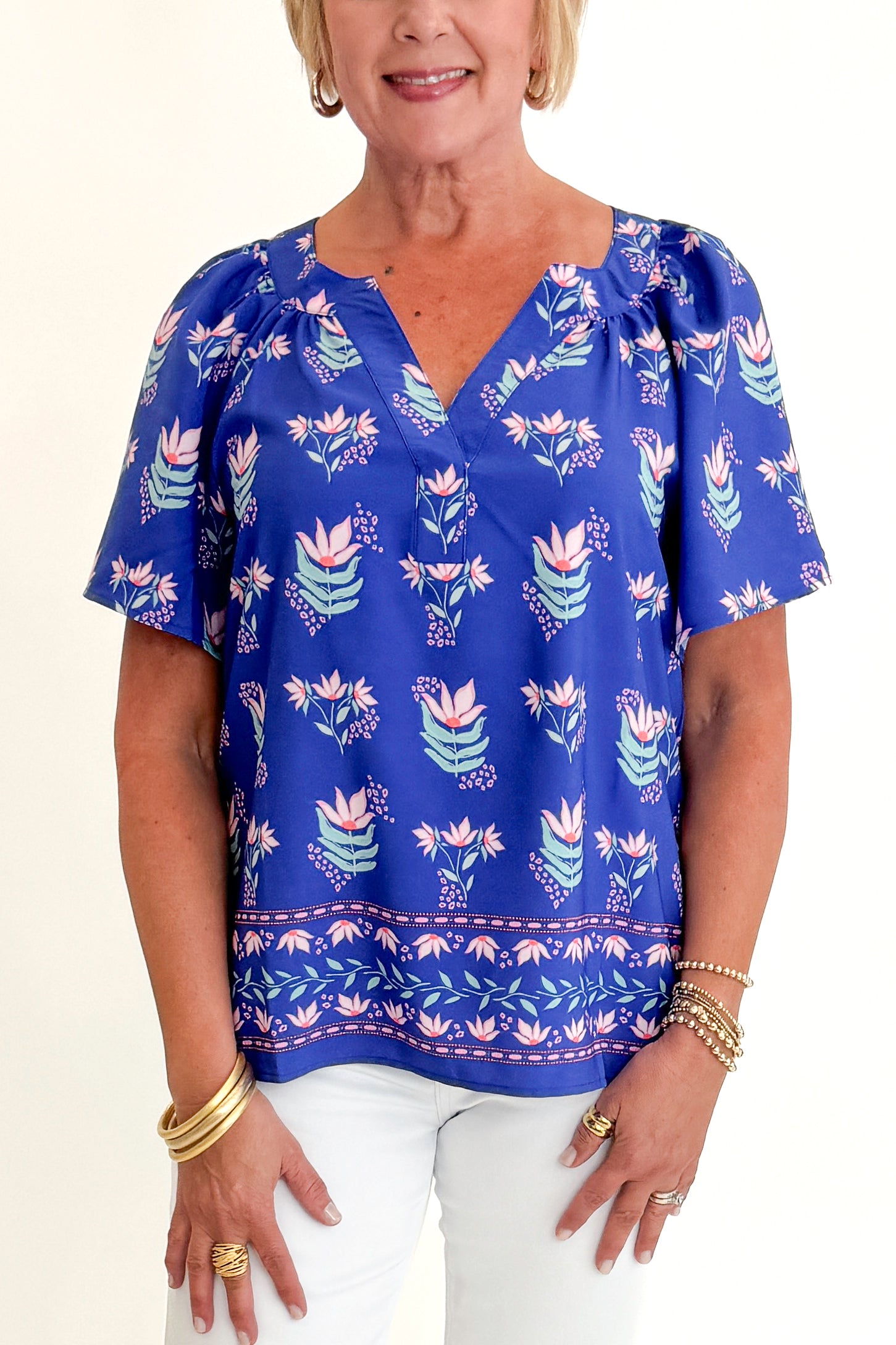 Front detail view of woman wearing Swagger Boutique’s Blue Petal Print Lori Top by Mary Square with white jeans against white studio background.