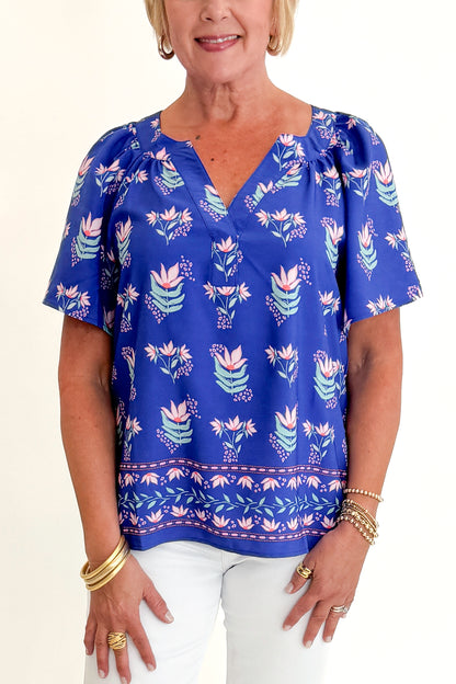 Front detail view of woman wearing Swagger Boutique’s Blue Petal Print Lori Top by Mary Square with white jeans against white studio background.