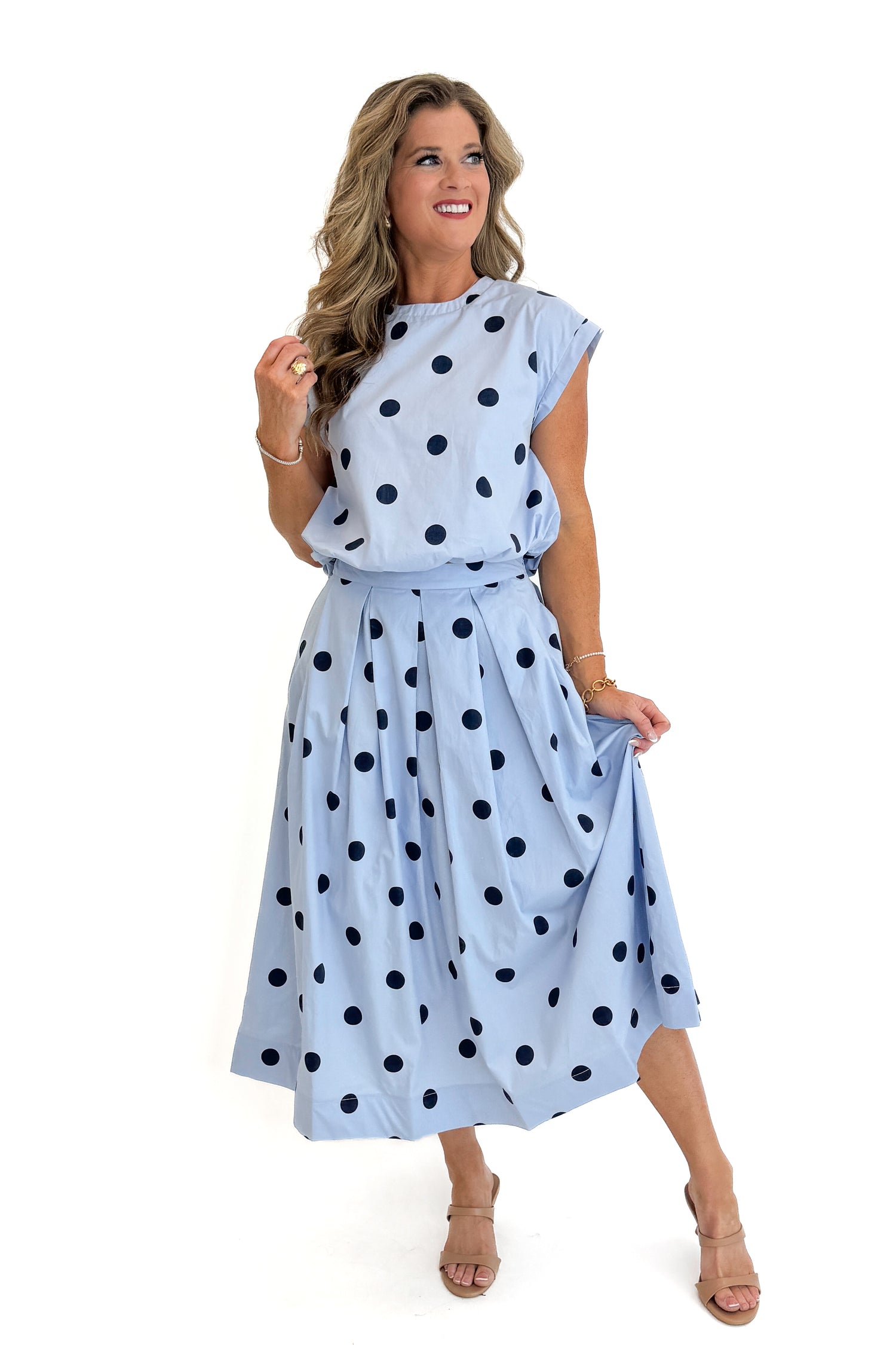 Front view of woman wearing Swagger Boutique’s Blue Polka Dot Bubble Hem Tank with matching Blue Polka Dot Pleated Midi Skirt against white studio background.