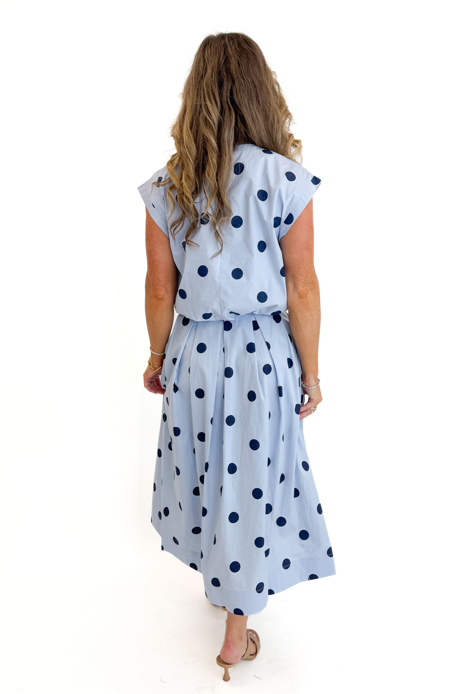 Back view of woman wearing Swagger Boutique’s Blue Polka Dot Bubble Hem Tank with matching Blue Polka Dot Pleated Midi Skirt against white studio background.