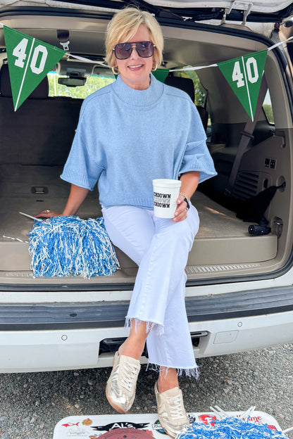 Front view of woman wearing Swagger Boutique’s Blue Ribbed Detail Short Sleeve Sweater with jeans sitting on a tailgate.