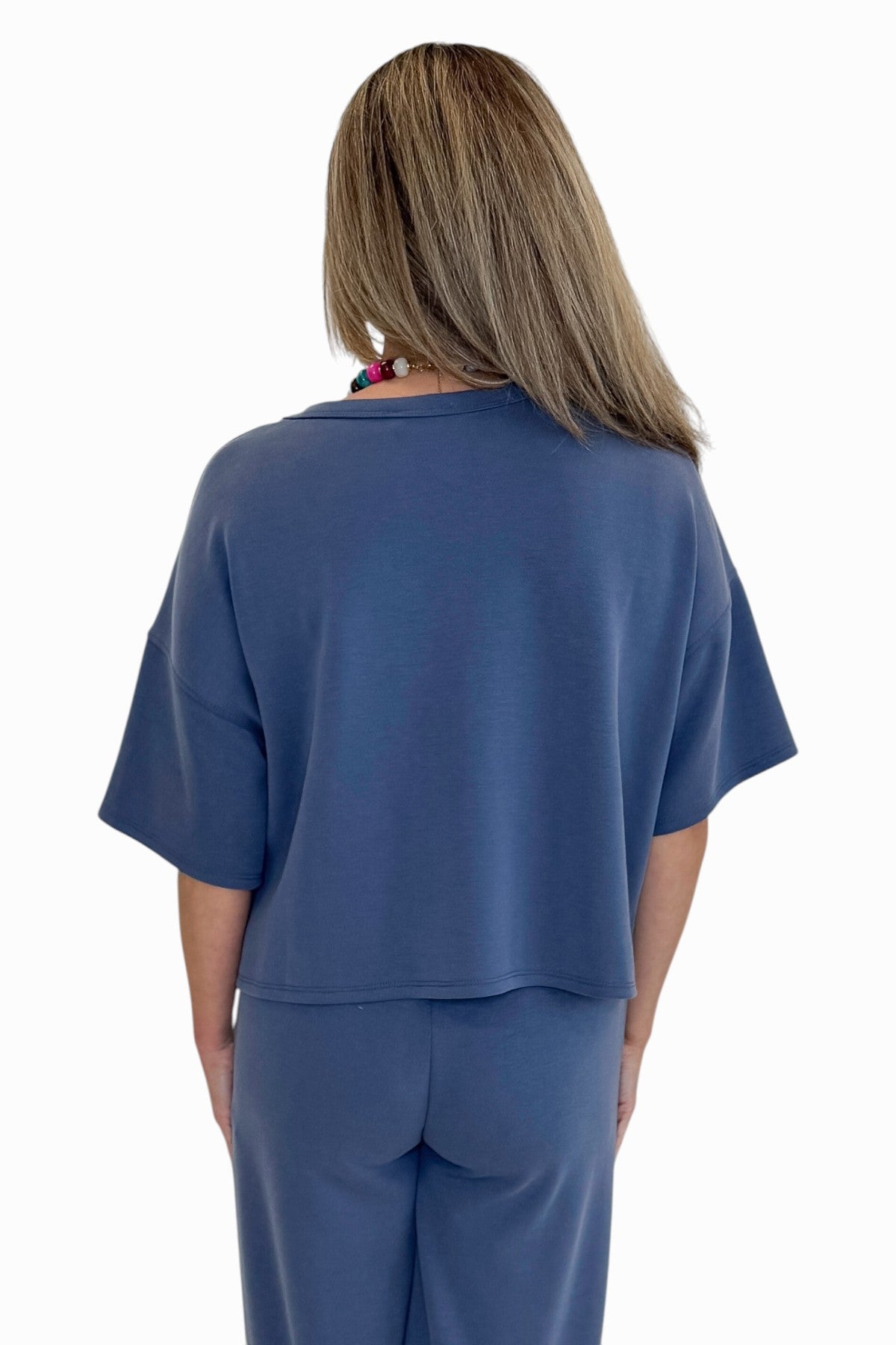 Back view of woman wearing Swagger Boutique’s Blue Cropped Lounge Pants and matching Blue Round Neck Short Sleeve Top against white studio background.