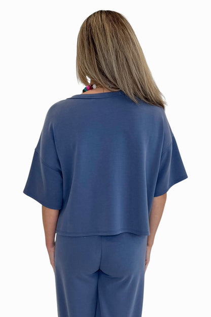 Back view of woman wearing Swagger Boutique’s Blue Cropped Lounge Pants and matching Blue Round Neck Short Sleeve Top against white studio background.