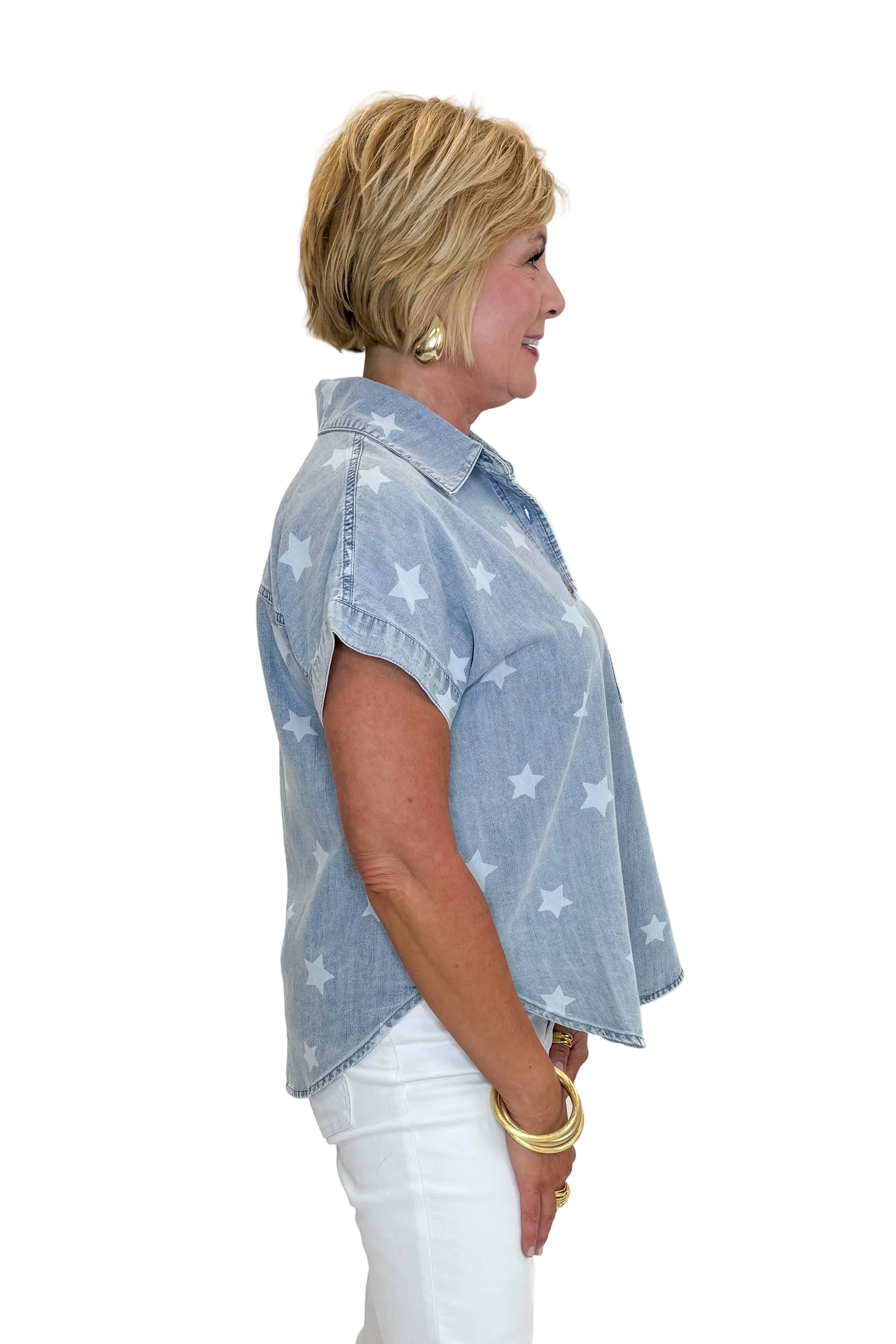 Side view of woman wearing Swagger Boutique’s Spark After Dark Blue Star Print Denim Top with jeans against white studio background.