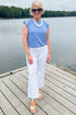 Front view of woman wearing Swagger Boutique’s Blue Striped Bubble Hem Sleeveless Top with jeans standing on a dock outside.