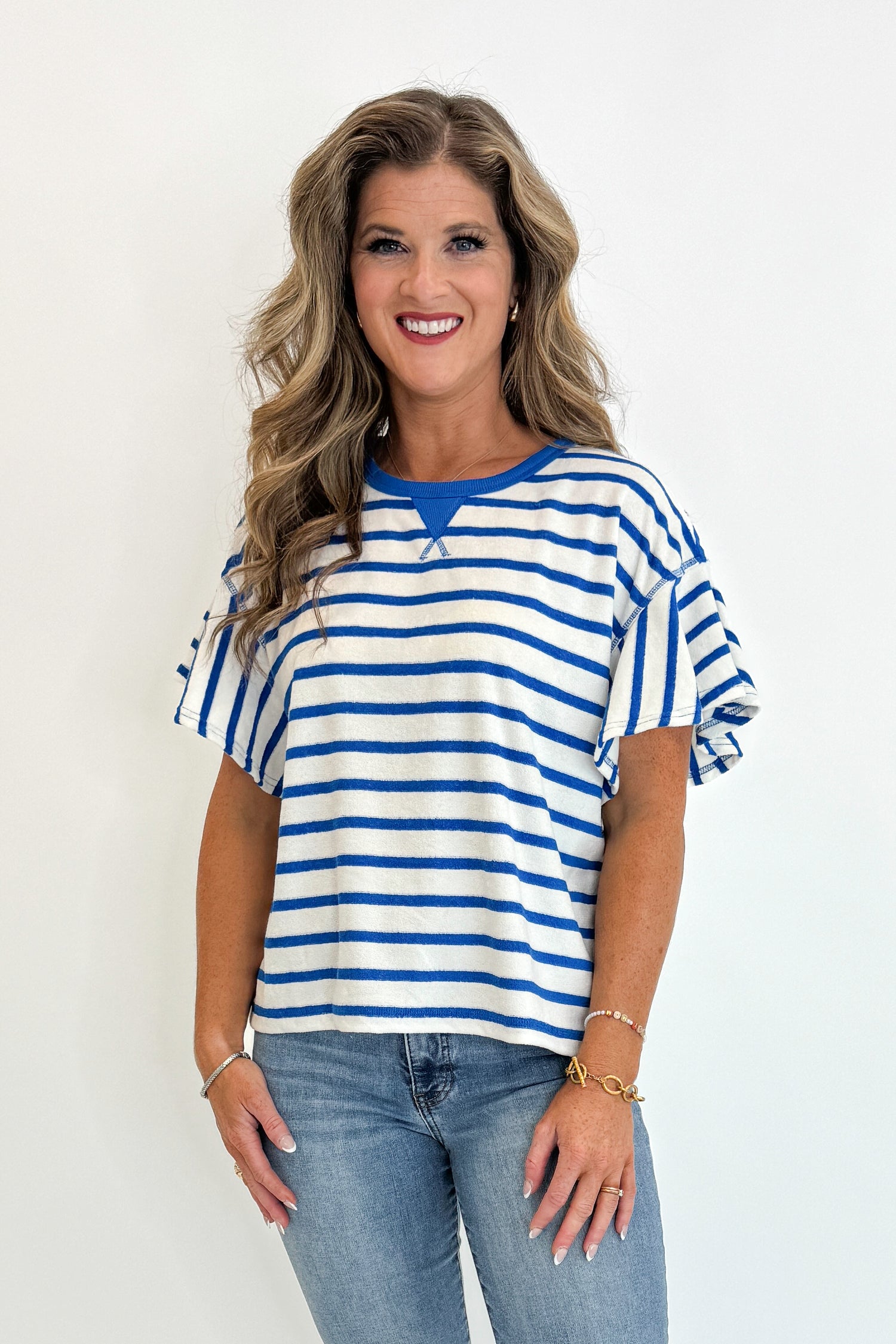 Front view of woman wearing Swagger Boutique’s Striped Flutter Sleeve Terry Top with jeans against white studio background.