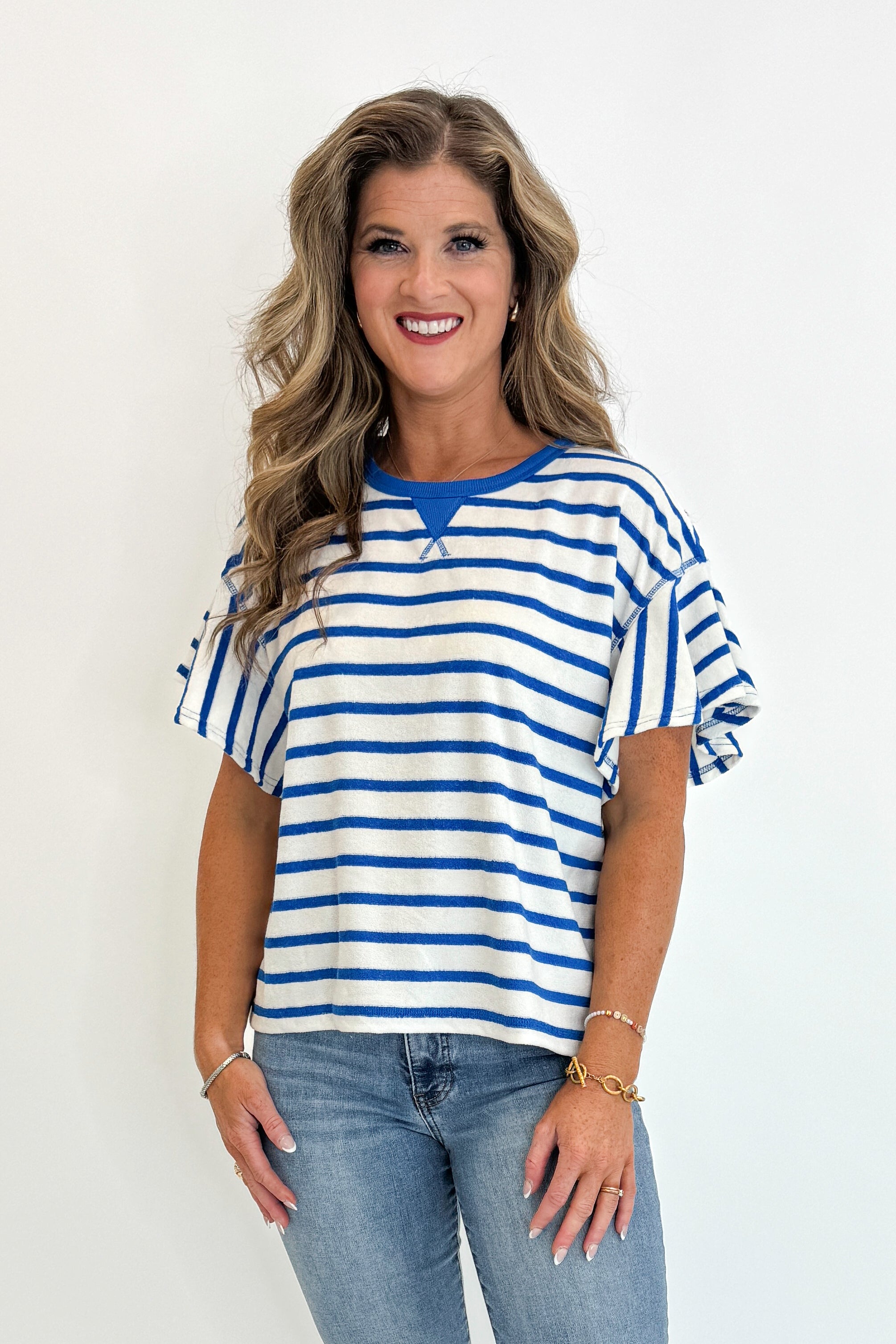 Front view of woman wearing Swagger Boutique’s Striped Flutter Sleeve Terry Top with jeans against white studio background.