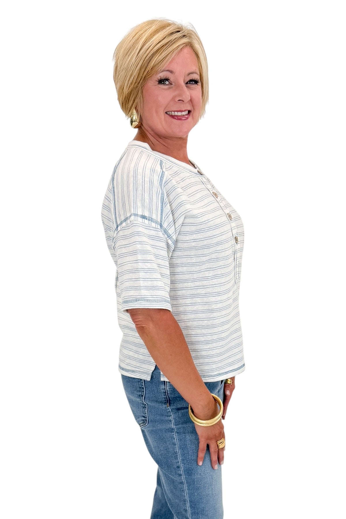 Side view of woman wearing Swagger Boutique’s Blue Striped Relaxed Fit Top with jeans against white studio background.