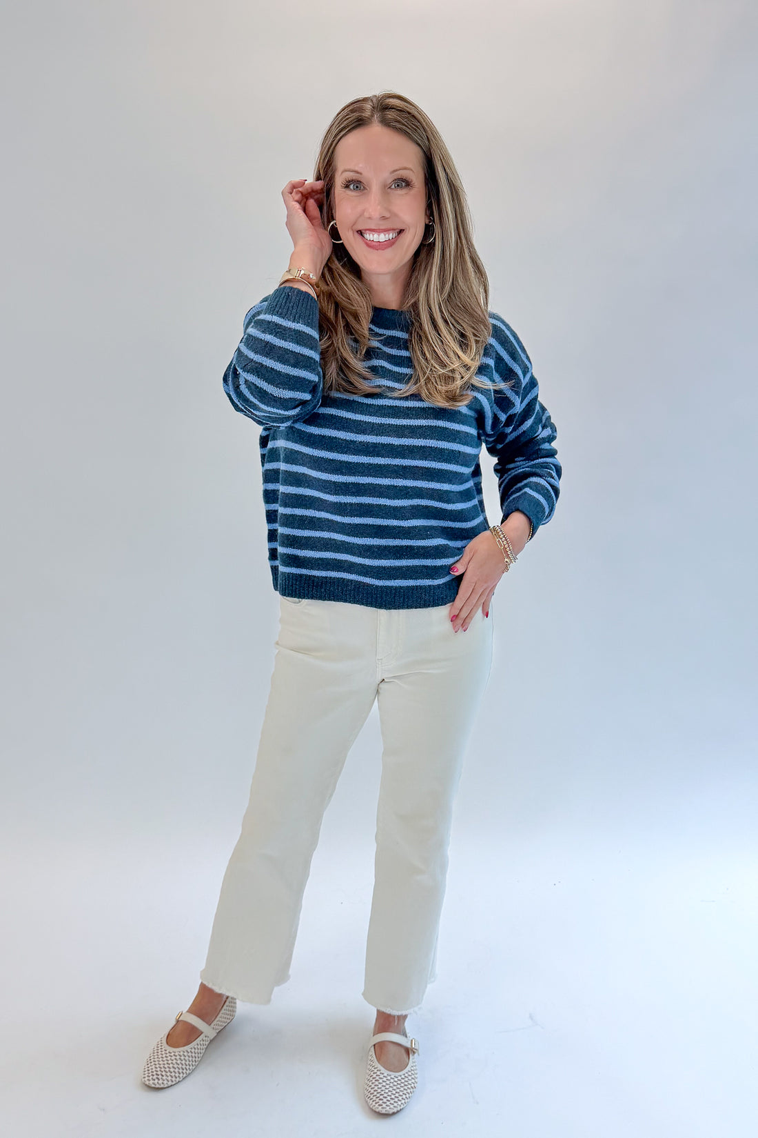Front view of woman wearing Swagger Boutique’s Blue Striped Sweater with jeans against white studio background.