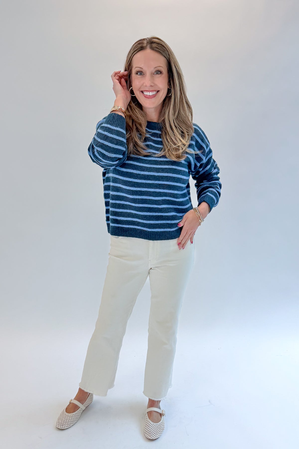 Front view of woman wearing Swagger Boutique’s Blue Striped Sweater with jeans against white studio background.