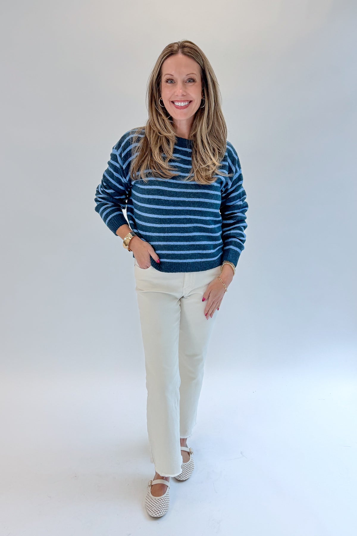 Front view of woman wearing Swagger Boutique’s Blue Striped Sweater with jeans against white studio background.