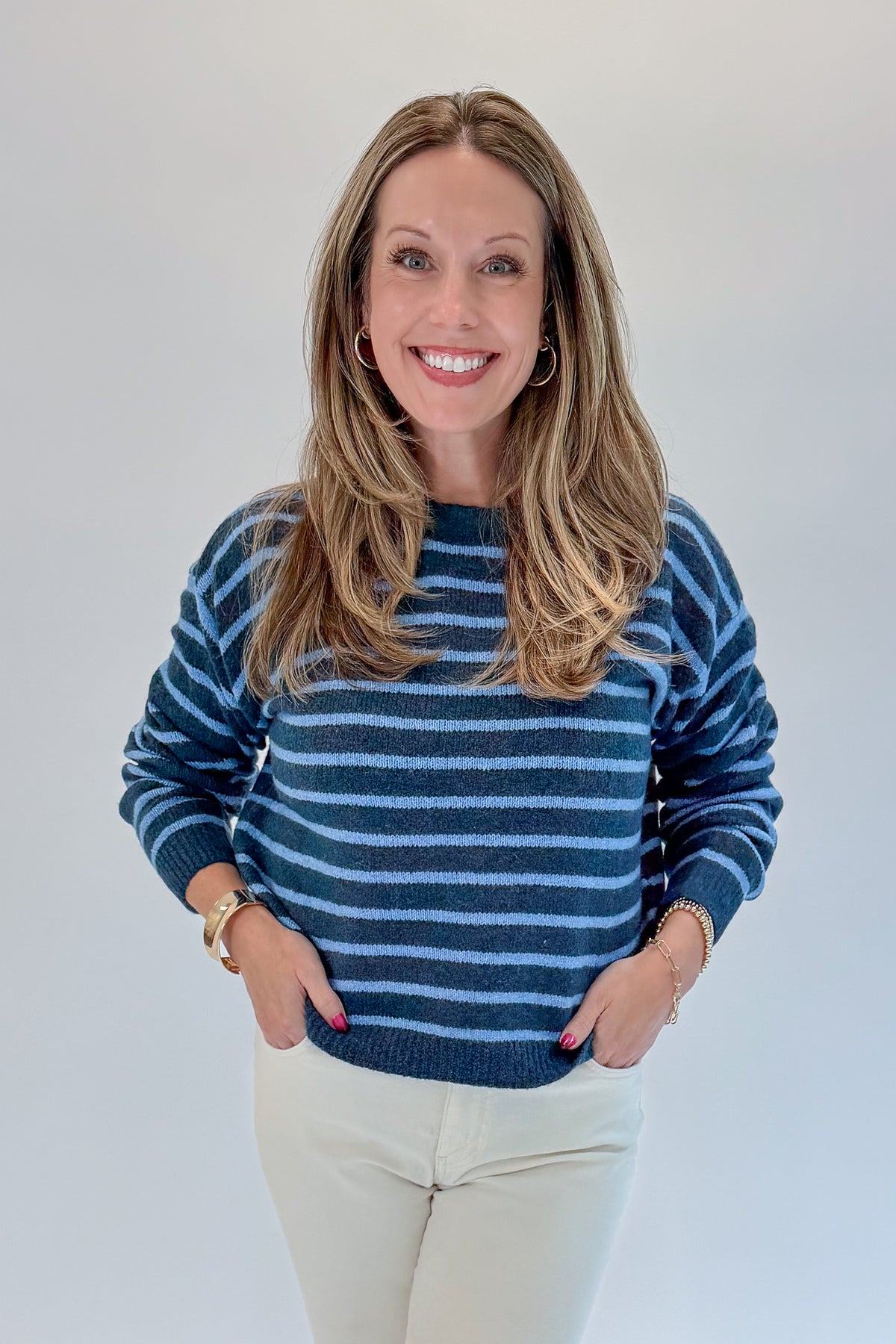 Front view of woman wearing Swagger Boutique’s Blue Striped Sweater with jeans against white studio background.