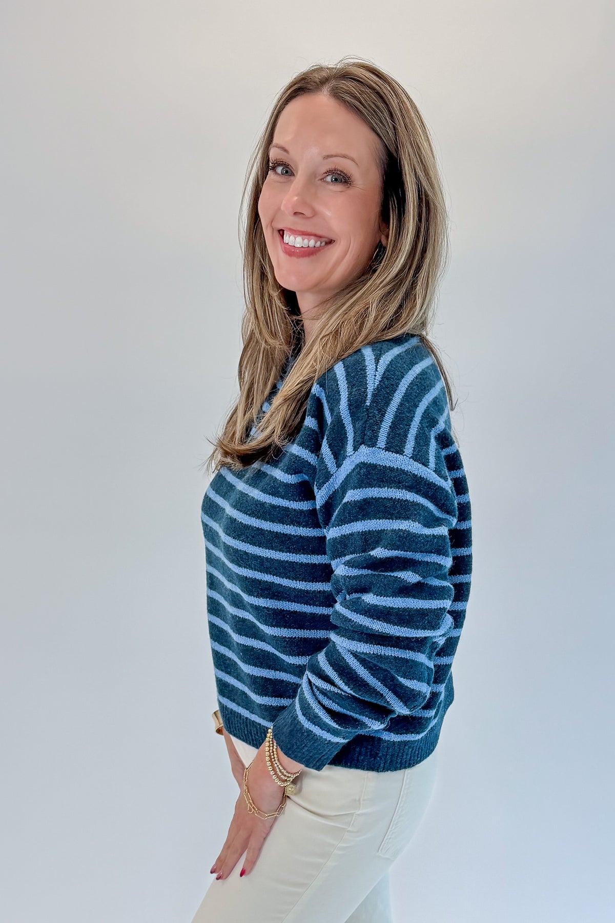Side view of woman wearing Swagger Boutique’s Blue Striped Sweater with jeans against white studio background.